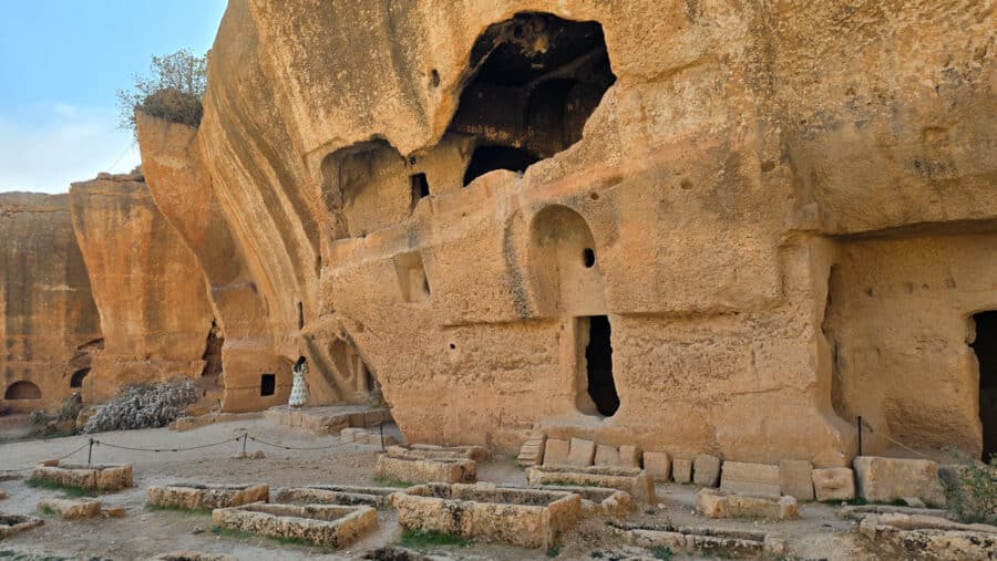 Nestled in the heart of Mardin, Turkey, these ancient rock-cut caves with carved openings and steps stand as a testament to Mesopotamian heritage. Surrounded by stone remains and a sandy pathway, they whisper the stories of an ancient city long past.