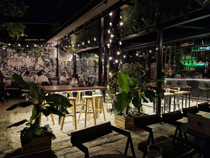 In the heart of Belgrade's nightlife, this outdoor bar features high tables and stools, enveloped by lush plants and twinkling string lights. People gather in the backdrop near a graffiti-styled wall, making it one of the must-visit places to party.