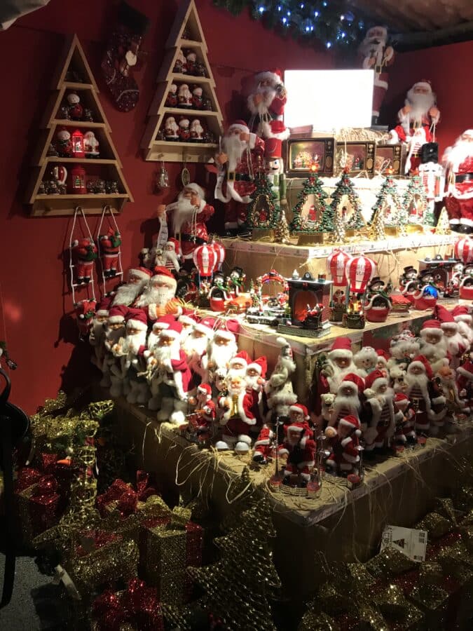 A festive display with numerous Santa Claus figurines, Christmas trees, ornaments, and gift boxes arranged on shelves against a red backdrop captures the enchanting spirit of Christmas in Istanbul.