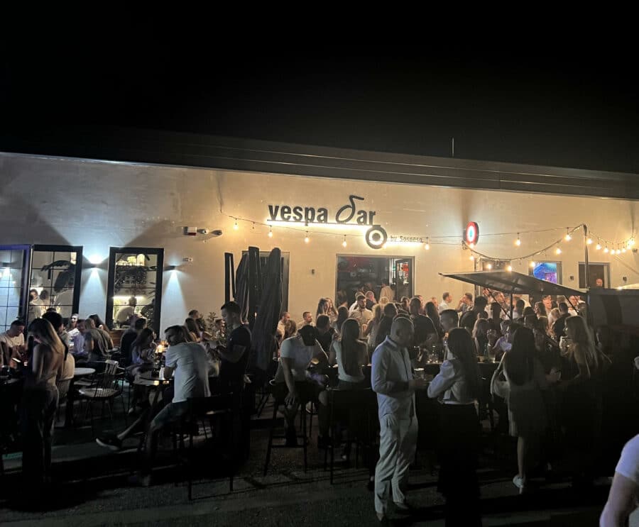 A lively crowd gathers outside Vespa bar at night, under string lights, embracing the vibrant Belgrade nightlife in a social atmosphere.