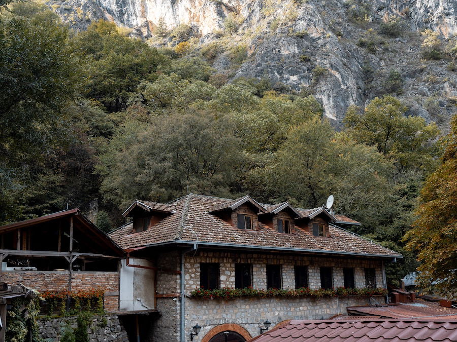 Nestled among dense trees, a stone building with a tiled roof stands against the backdrop of rocky cliffs. This enchanting scene captures the essence of Matka Canyon near Skopje, inviting visitors to explore its natural beauty and history. Discover more with a full guide to this breathtaking destination.