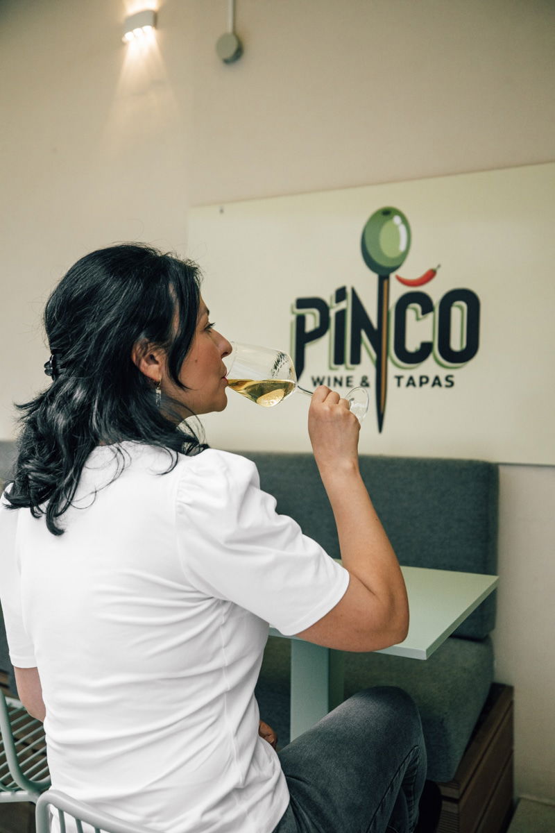 A person sits at a table inside Pinčo Tapas & Wine Bar in Zadar, enjoying a glass of white wine.